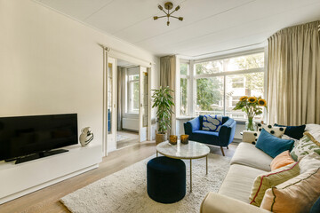 A stylish modern living room featuring a mix of comfortable furniture, large windows, and indoor plants, creating a warm and inviting atmosphere.