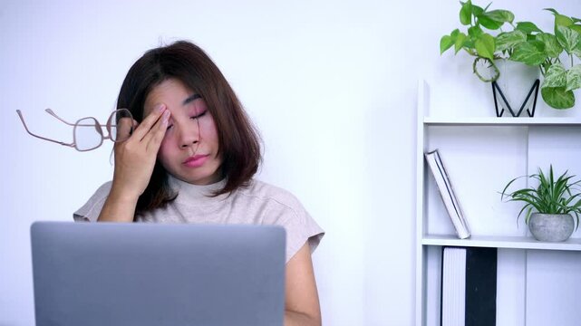asian woman removing her eyeglasses due to eye pain, blurred vision, headache, and fatigue, using her hand to rub her eyes and temples after prolonged screen time or eye strain