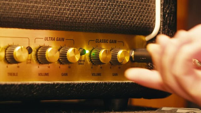 Close-up of plugging a jack into a guitar amplifier and turning up the volume knob, live concert show, playing music on guitar tube amplifier.