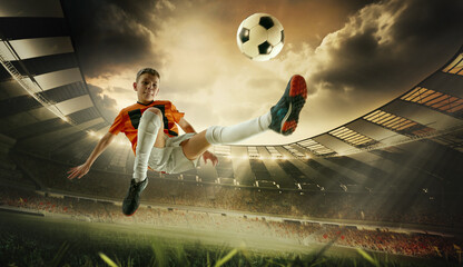 Naklejka premium Young soccer player in orange jersey kicking ball midair with focused expression during night match. 3D render of open air stadium. Concept of sport, energy, skill, tournament, competition.
