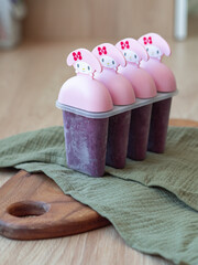 A pink popsicle mold set with homemade berry ice cream standing on a green napkin and wooden cutting board 