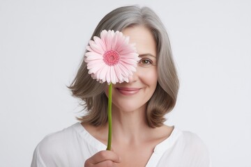 Smiling Mature Woman Holding Pink Gerbera Flower Covering One Eye with Soft Light