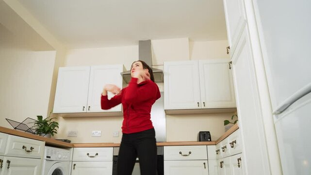 Energetic woman dancing wildly in kitchen. Person feeling energy and dancing with funny movements. Lively female moving enthusiastically letting loose enjoying home atmosphere