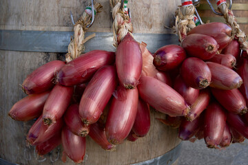 Shiny red onions with smooth elongated shapes are tied together in a dense bunch with visible outer...