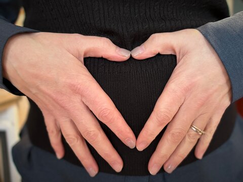 Forme de c&oelig;ur r&eacute;alis&eacute;e avec les mains sur le ventre d'une femme portant un pull noir