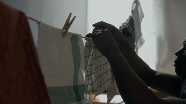 Close-up shot of middle-aged African American man hanging washed towels on clothesline in cozy lived-in apartment