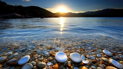 Obraz premium Serene sunrise over tranquil coastline. Crystal-clear water laps gently over smooth, colorful pebbles. Golden sunlight illuminates the scene
