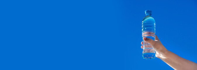 A girl holds a bottle of drinking water in her hand against a blue sky background
