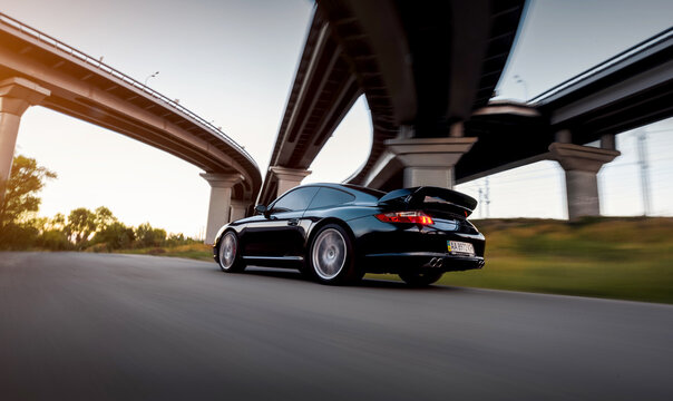 Motion shot of black Porsche 911 Carrera coupe. Rear three quarter view of Porsche 997 driving under a highway interchange at sunset. Kyiv, Ukraine - September 18 2016.