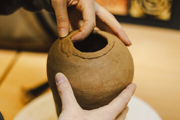 Hands skillfully shape a clay pot in a pottery studio. The workshop encourages creativity and...