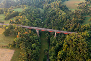 Fototapeta premium Aerial view at sunrise of a train bridge over a river surrounded by forest