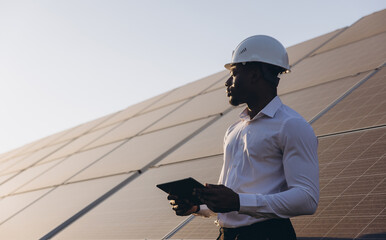 African American Engineer Inspecting Solar Panels with Digital Tablet at Sunset