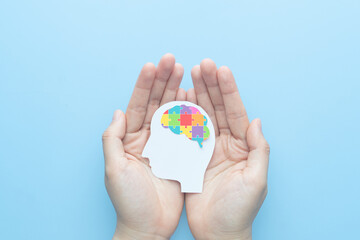World autism awareness day concept. Hands holding human head shape with colorful jigsaw puzzle brain on blue background. Creative idea for Autism Spectrum Disorder (ASD).