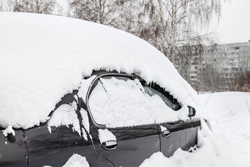 Passenger car covered with snow. Winter weather, snowfall. Abandoned car.