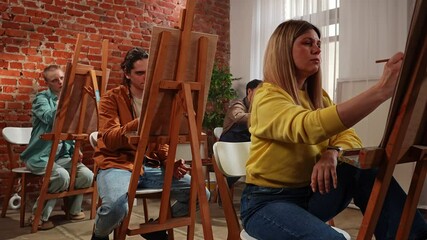 Group of adult people sitting at easels drawing pictures with pencils during master class in studio. Slow motion.