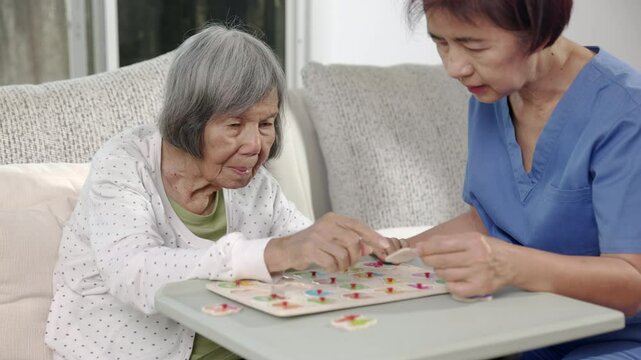 Nurse in nursing home helping a senior woman with number puzzle game. Dementia, Alzheimer's disease.