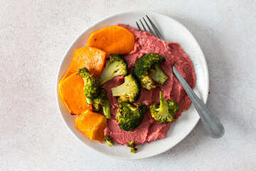 A healthy, balanced breakfast with beetroot hummus, roasted sweet potatoes, and broccoli, topped with a fresh pink radish and Chinese cabbage salad with chia seeds