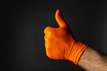 Thumbs up gesture with an orange glove on a dark background