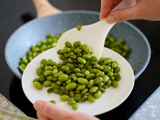 Woman putting freshly cooked green Edamame soy beans on to a plate from a frying pan
