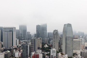 Obraz premium Foggy aerial view of Tokyo urban landscape from Tokyo Tower shows skyscrapers disappearing into the mist while dense architecture creates a layered and atmospheric cityscape