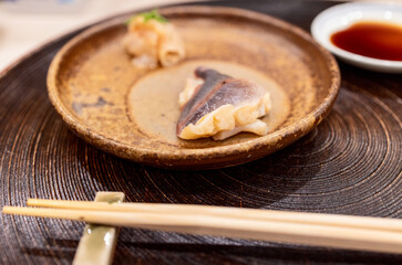 Surf clam sashimi presented on a rustic ceramic plate with a minimal garnish, captured with a bokeh effect highlighting the simplicity and refined aesthetics of Japanese cuisine