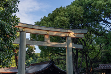 Traditional wooden torii gate at Meiji Shrine in Tokyo featuring three golden chrysanthemum ornaments symbolizing the imperial family framed by dense foliage