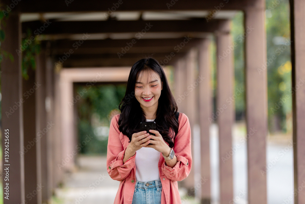 Poster happy asian student using smartphone while walking in university corridor