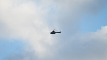 Military helicopter in the sky during flight against blue sky and gray clouds