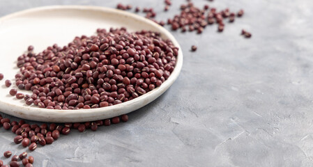 Plate full of dried red azuki beans on gray closeup. East Asian legumes, vegetarian protein source