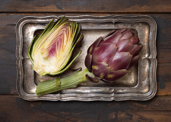 Half and whole purple raw roman artichokes on a dark wooden table top view. Fresh italian vegetables