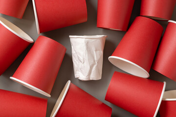 New red paper cups and crumpled used white one on a gray top view. Consumerism concept