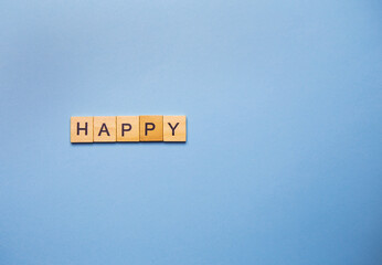 Wooden blocks spell out the word 'HAPPY' on a light blue background