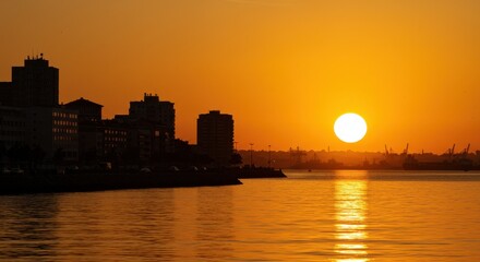 Obraz premium City skyline silhouette at sunset with buildings and water reflecting the golden light of the sun