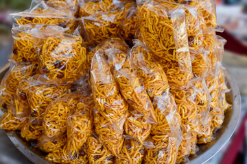 This image shows a metal tray filled with neatly arranged plastic bags of a popular Indian snack called Sev, or Mixture. The savory, crispy, spiced, golden-yellow fried noodles are mixed with peanuts.