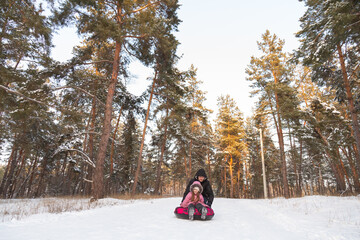 Father and daughter having fun with snow tube in the forest