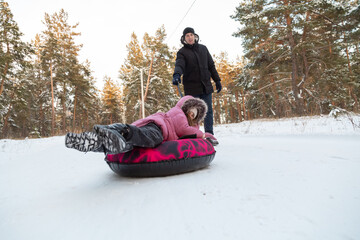Father and daughter having fun with snow tube in the forest