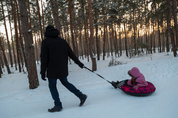 Dad with his daughter walking with snow tubing in the winter forest