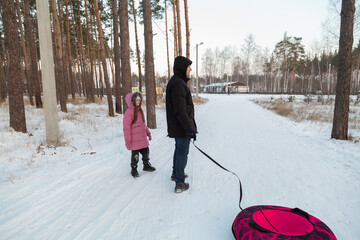 Dad with his daughter walking with snow tubing in the winter forest