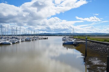 Fototapeta premium Docked boats in calm water, cloudy sky above, green land afar