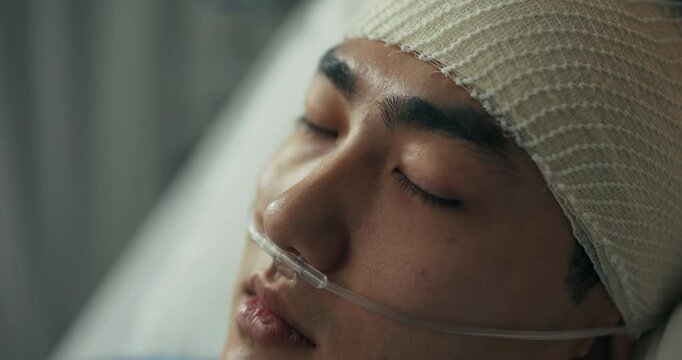 A young man undergoing medical care rests in a hospital ward, his head wrapped in bandages and an oxygen tube ensuring proper breathing as he slowly recovers from a critical condition.