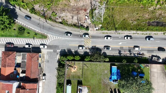 vis&atilde;o a&eacute;rea de uma avenida movimentada em regi&atilde;o residencial de mogi das cruzes, com ve&iacute;culos, casas, &aacute;rvores e fluxo urbano intenso