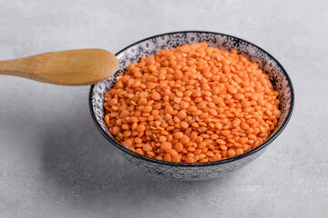 Raw red lentils in ceramic bowl on a light gray table, selective focus. Legume for healthy balanced diet, plant-based protein source