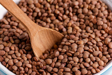 Organic brown lentil with wooden spoon, close up texture, legumes for vegan and vegetarian cooking, pulses for healthy balanced diet, plant-based protein source