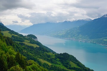 Green hills overlook a blue lake with cloudy mountains backdrop