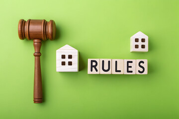 Real Estate Rules Concept – Wooden Gavel and House Models on Green Background