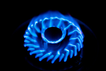 A gas stove burner with a bright blue flame, glowing against a dark backgroundA gas stove burner...