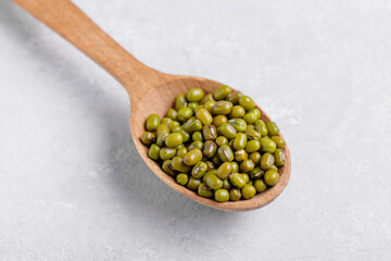 Organic mung beans in a wooden spoons on grey table background. Healthy plant-based protein, healthy cooking ingredient for vegan recipes and vegetarian diets