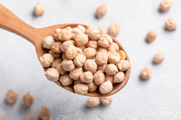 Organic chickpeas on wooden spoon on grey table background. Healthy plant-based protein, healthy cooking ingredient for vegan recipes and vegetarian diets