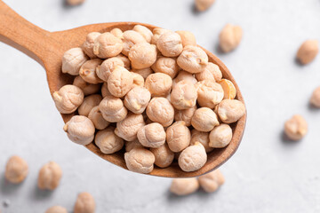 Raw chickpeas on wooden spoon on grey table background. Healthy plant-based protein, healthy cooking ingredient for vegan recipes and vegetarian diets, close up