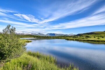 Lake reflects sky near mountains. Greenery lines shore, sunny day